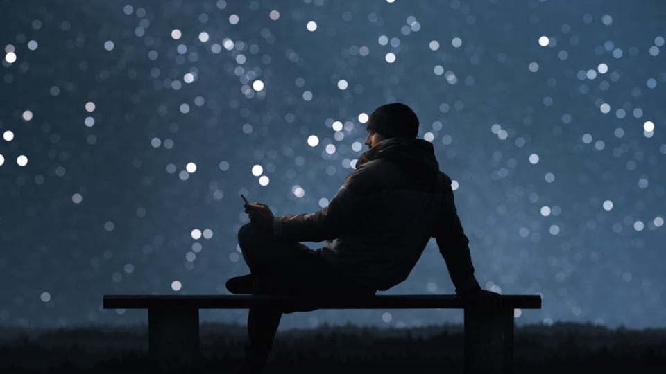 Mann sitzt or Sternenhimmel auf einer Bank und schaut auf ein Handy