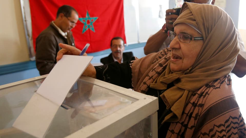 Frau wirft Zettel in Wahlurne.