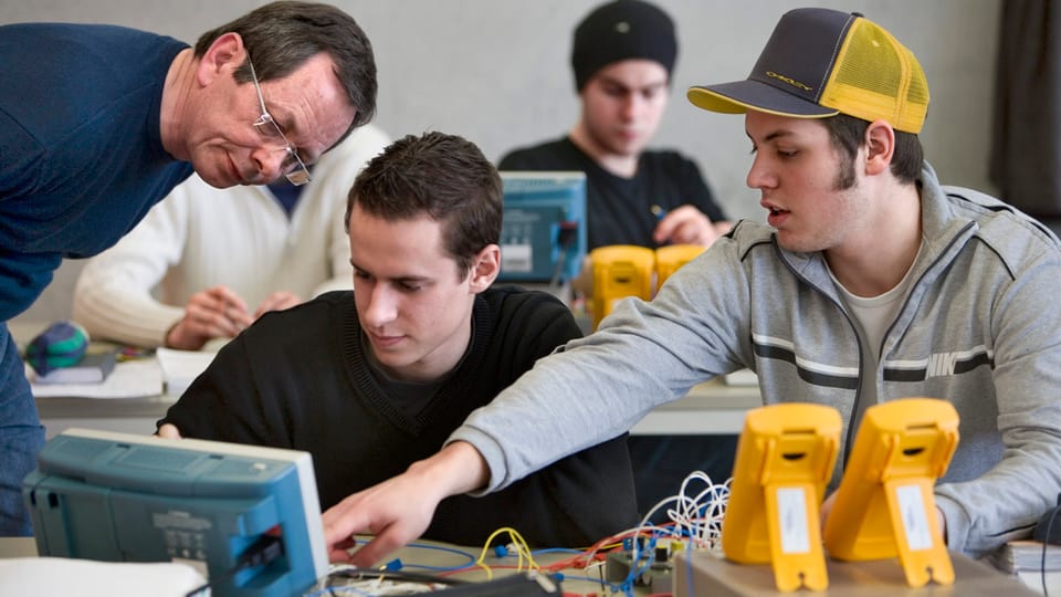 Junge Männer in der Berufsschule mit allerlei technisch-elektronischem Gerät auf dem Tisch.
