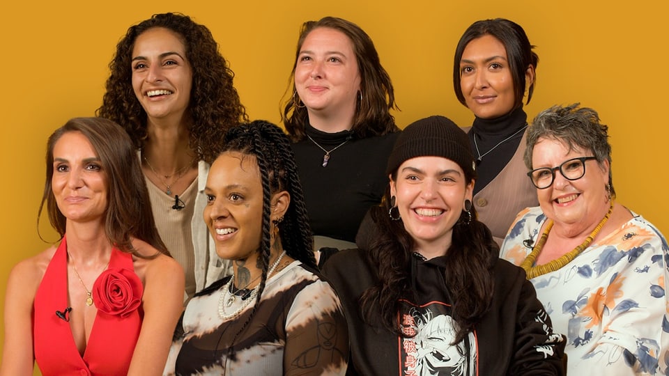 Sieben Frauen posieren vor einem gelben Hintergrund.