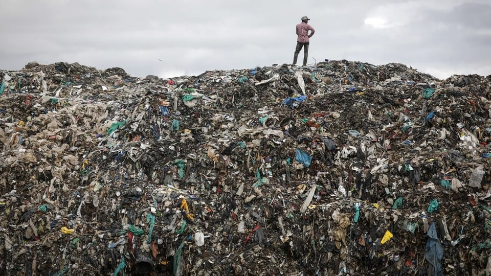 A man stands on top of a pile of garbage at the Dandora landfill in Nairobi, Kenya.