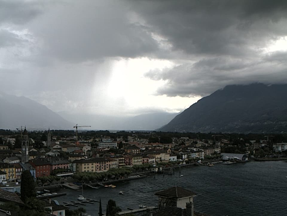 Blick auf die Seepromenade von Ascona und die Magadinoebene. In der linken Bildhälfte ist der bindfädenartiger Gewitterregen zu sehen.
