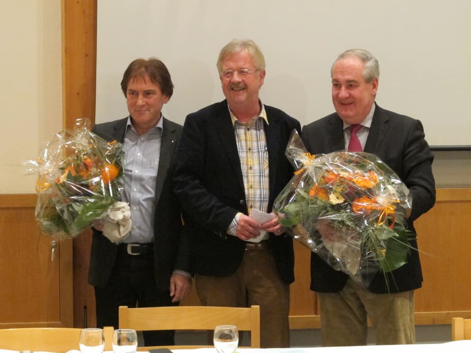 Hubert Bläsi, Claude Barbey und Boris Banga strahlen in die Runde. Bläsi und Banga halten je einen Blumenstrauss. 