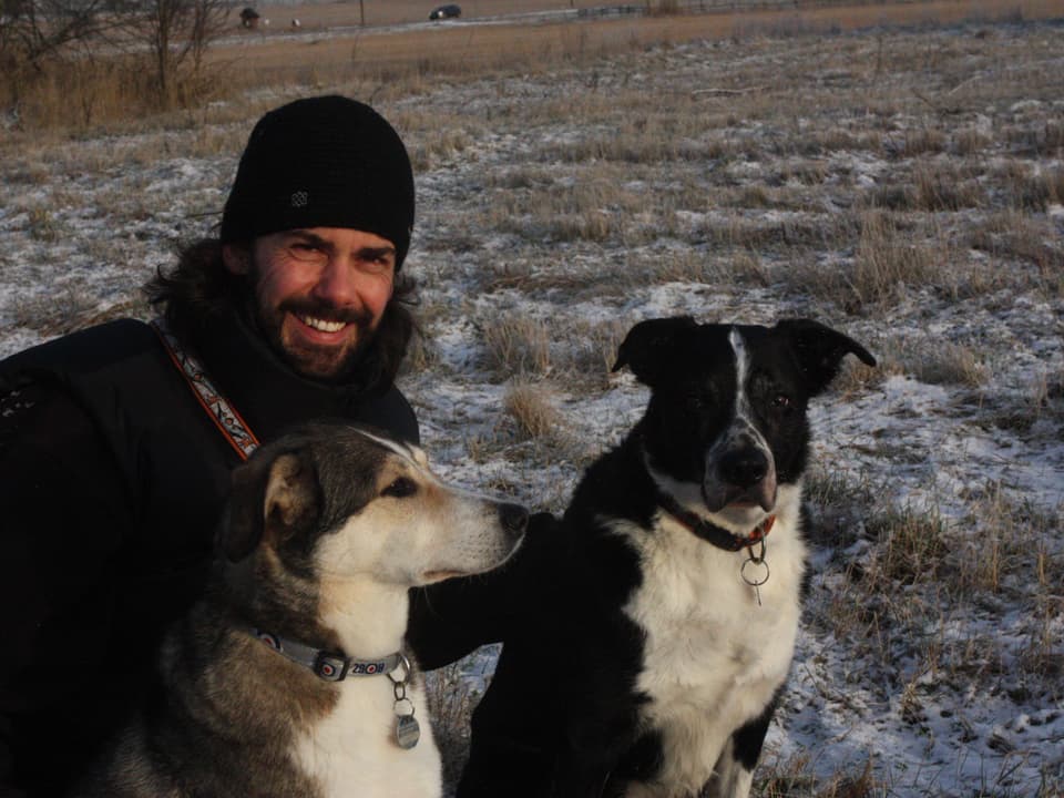 Olaf Thalmann mit zwei Hunden auf einem Feld.