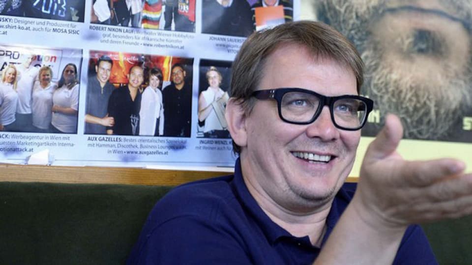 Sven Regener sitzt vor einem Plakat und ist lachend in ein Gespräch vertieft.