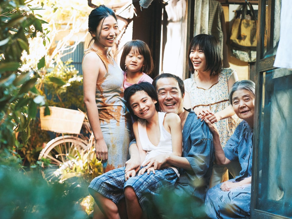 Eine sechsköpfige Familie sitzt lachend vor einem Haus