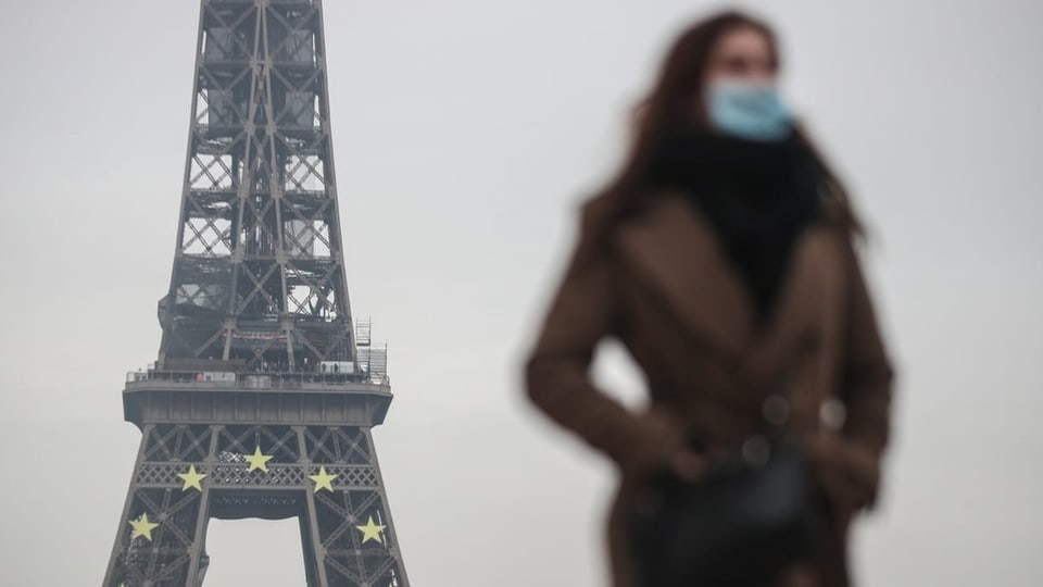 Eine Frau mit Maske vor dem Eiffelturm