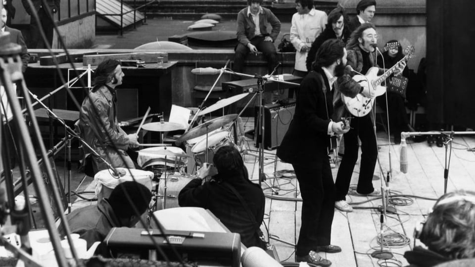 Die Beatles auf einem Dach umgeben von weiteren Personen.