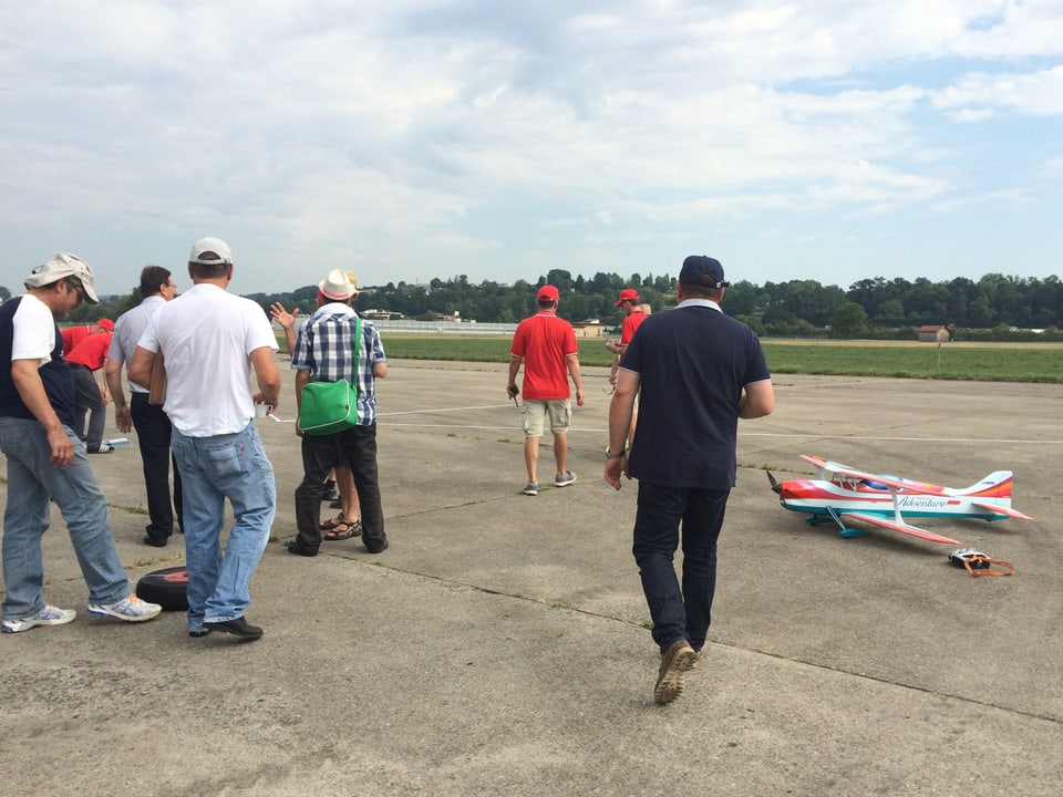 Männer stehen auf einer Startbahn um ein Modellflugzeug herum.
