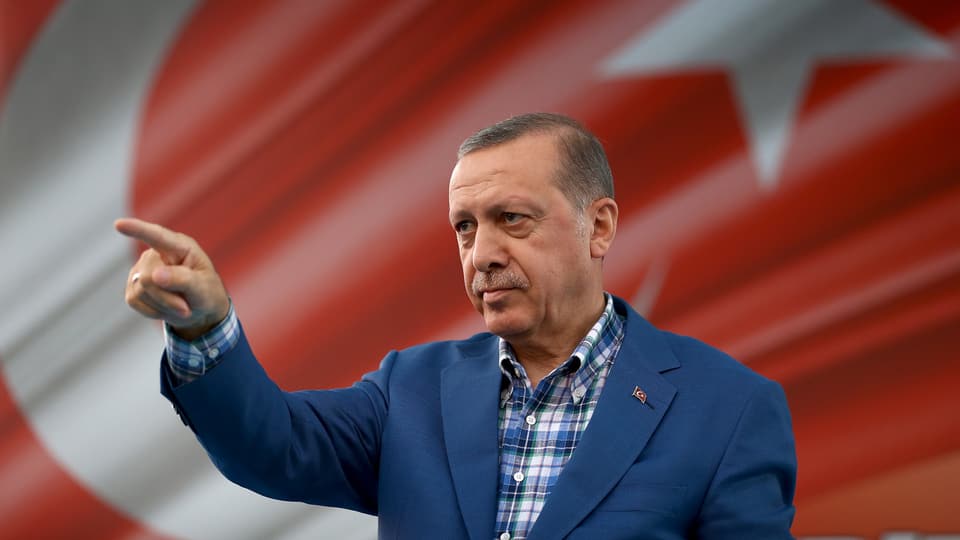 Erdogan mit erhobenem Zeigefinger vor einer türkischen Flagge.