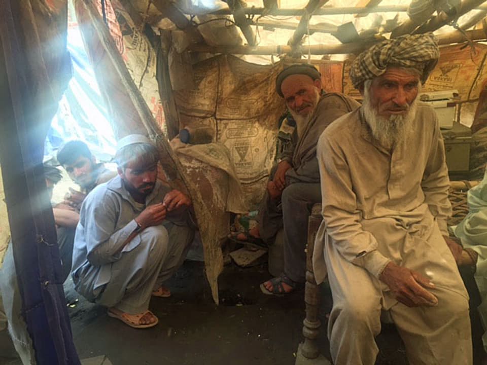 Vier afghanische Flüchtlinge sitzen unter Plachen in einem Zelt. Sie tragen alle Bärte und Gewänder.