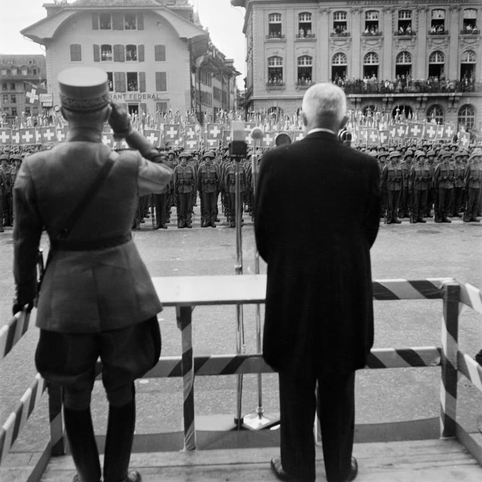Blick von hinten auf General Henri Guisan auf dem Berner Bundesplatz. Vor ihm stehen viele Soldaten in Reih und Glied.