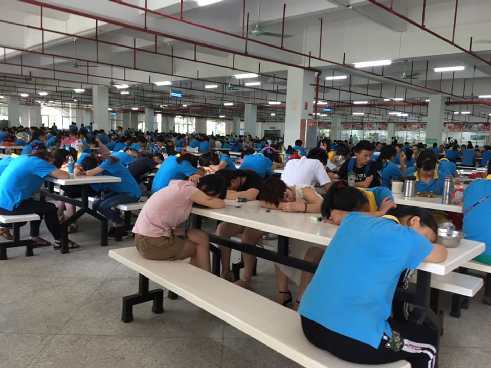 Chinesische Arbeiter mit Kopf auf dem Tisch in einer riesigen Kantine.