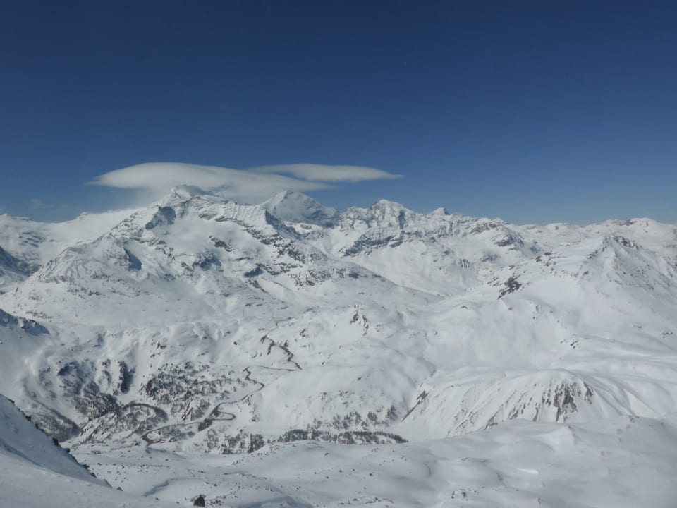 Schneebedeckte Berge und blauer Himmel. An einem Berg bildete sich eine linsenförmige Wolke.