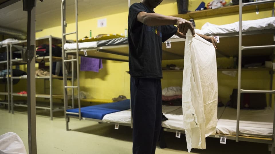 Ein Asylsuchender faltet ein Laken in einer Asylnotunterkunft.