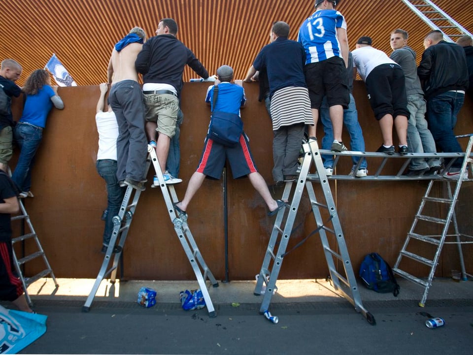 Zaungäste schauen auf Leitern ins Stadion
