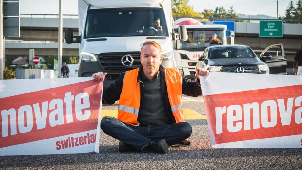 Ein Mann sitzt auf der Strasse und hält mit jeder Hand ein Banner