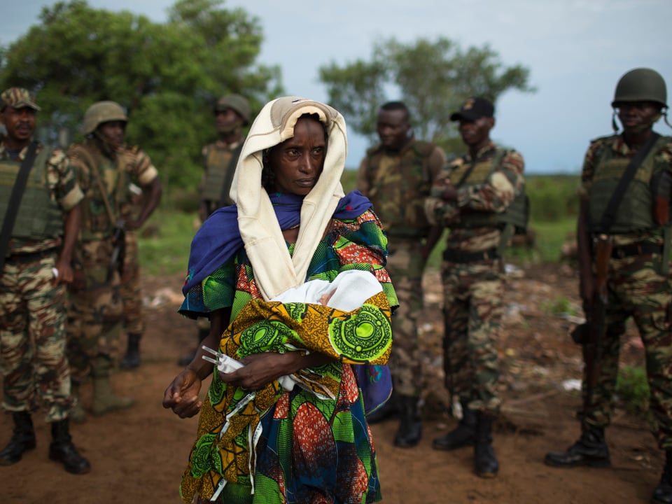 Eine Mutter mit ihrem Neugeborenen, beobachtet von Soldaten.