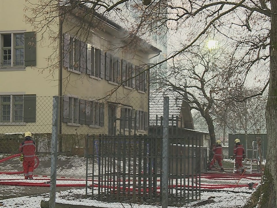 Vor dem Kindergarten stehen Feuerwehrleute mit roten Schläuchen.