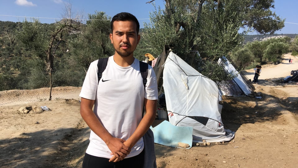 Junger Mann mit weissem T-Shirt, der vor einem kaputten Zelt steht.