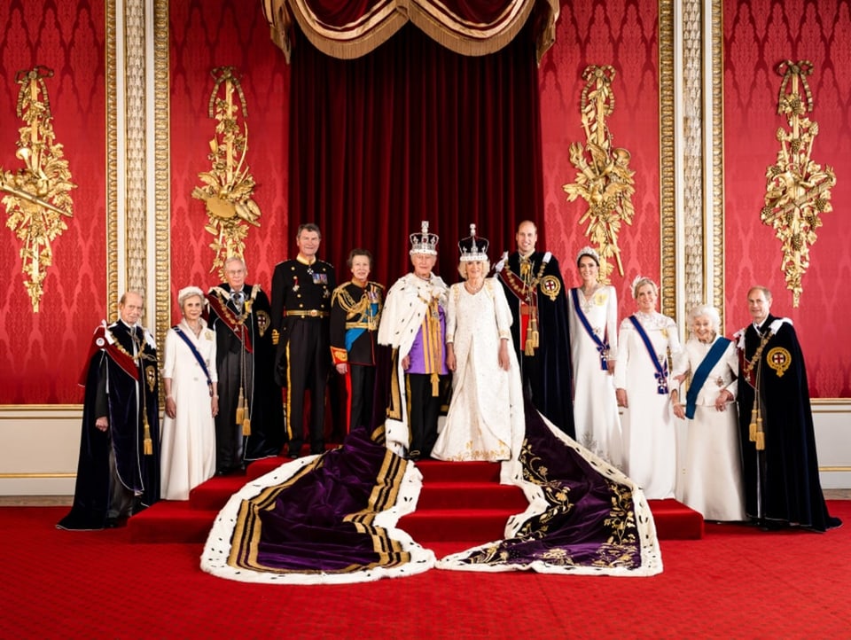 Auf dem Foto sind mehrere Mitglieder der Royal Family auf den Stufen des Throns zu sehen. Im Zentrum das Königspaar.