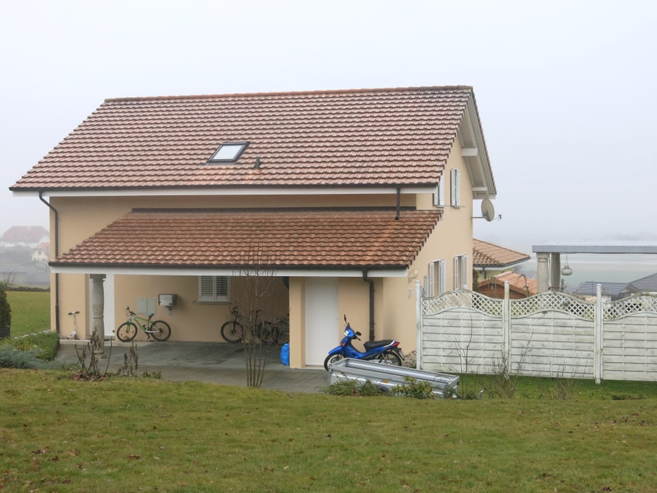 Ein einfaches, neueres Einfamilienhaus, davor stehen Veolos und Mopeds.