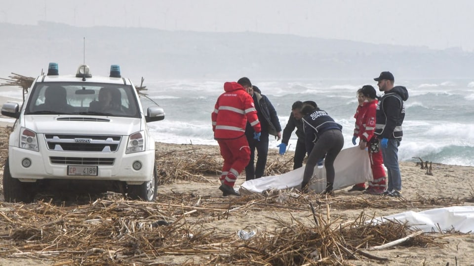 Rettungskräfte an Strand bergen die Leichen aus den Trümmern.