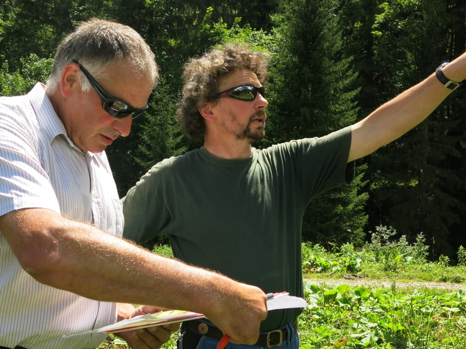 Kontrolleur Martin Rubin mit Älpler Hans Wüthrich, beide tragen Sonnenbrille, schauen auf Karte und Wiese.
