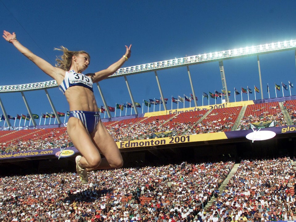 Blick auf die Zuschauerränge im Commonwealth Stadium von Edmonton, im Vordergrund eine Weitspringerin, die durch die Luft fliegt.