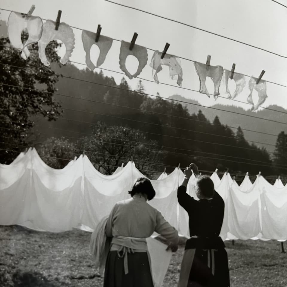 Zwei Frauen hängen Wäsche in ländlicher Umgebung auf.