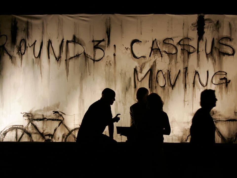 Silhouetten von Menschen sind vor einem Schiffcontainer zu sehen, der mit «Round 3: Cassius Moving» besprayt ist.