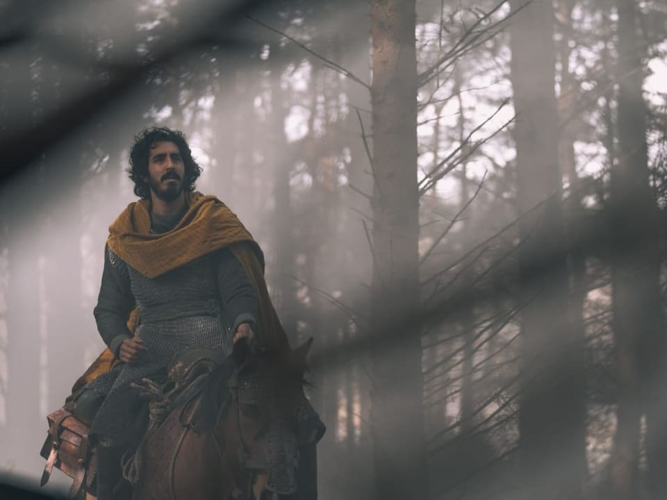Dev Patel (Sir Gaiwan) reitet auf einem Pferd durch den Wald. Er trägt Rüstung und einen grossen gelben Umhang.