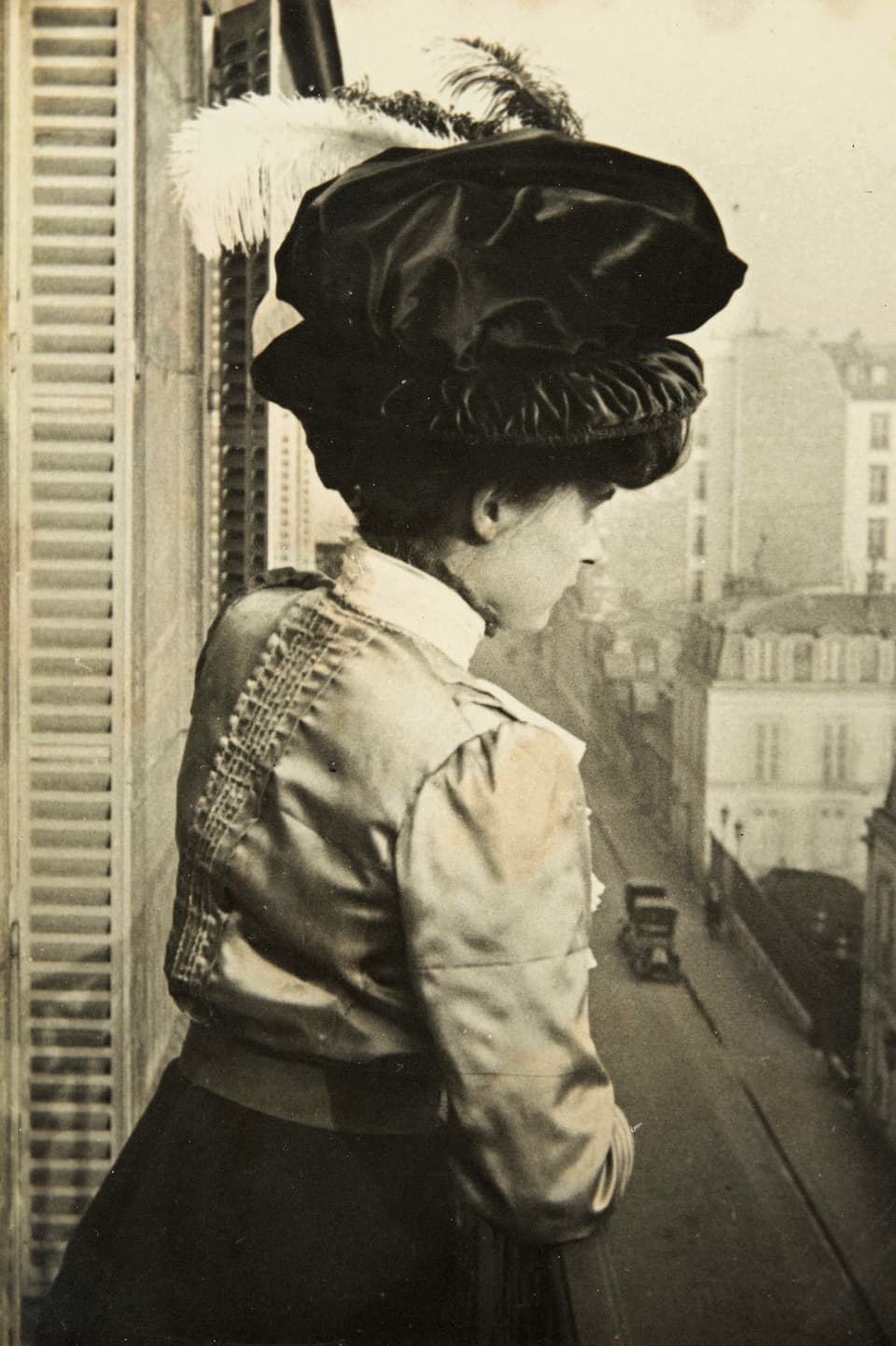 Alte Schwarzweissfotografie: Junge Frau mit der Federhut auf einem Balkon.