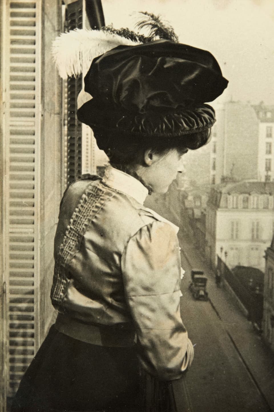 Alte Schwarzweissfotografie: Junge Frau mit der Federhut auf einem Balkon.