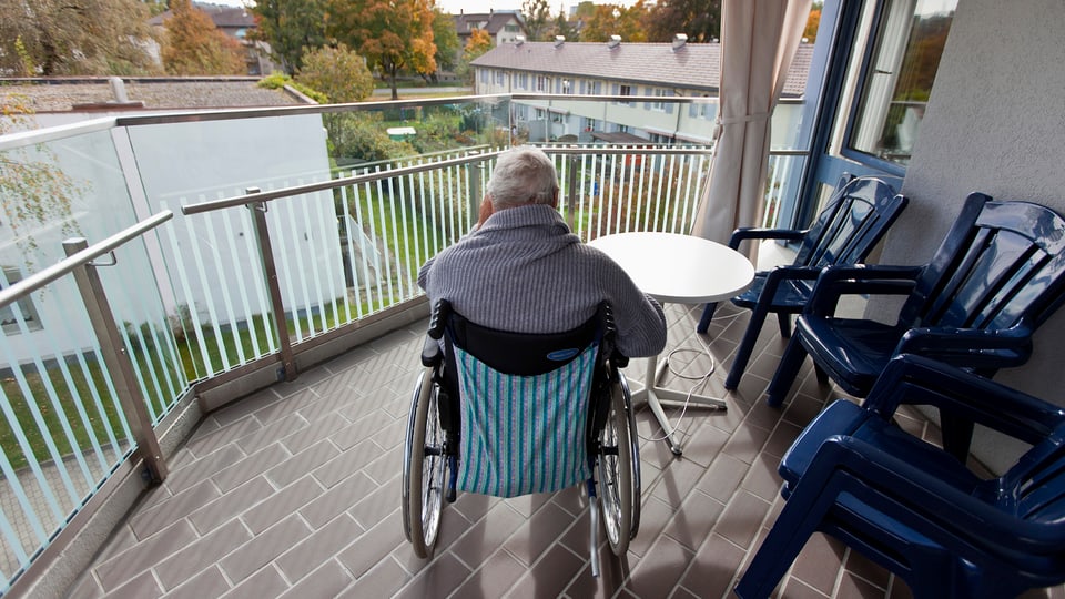 Eine Person sitzt auf dem Balkon im Rollstuhl
