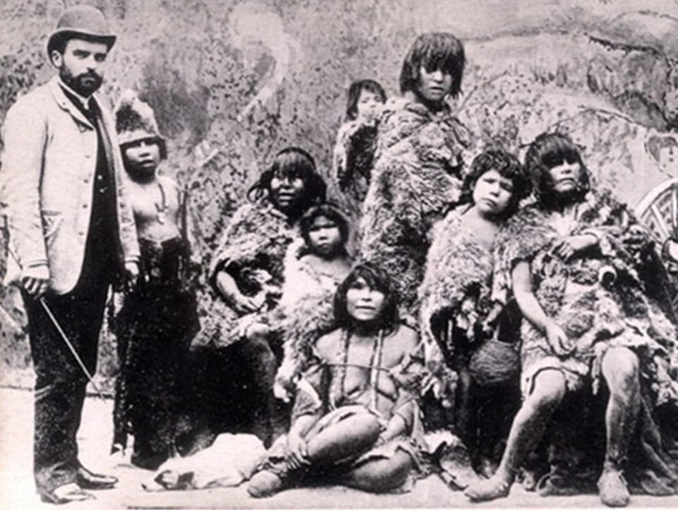 Weisser Mann mit Stock posiert neben Indigenen in Fellkleidung