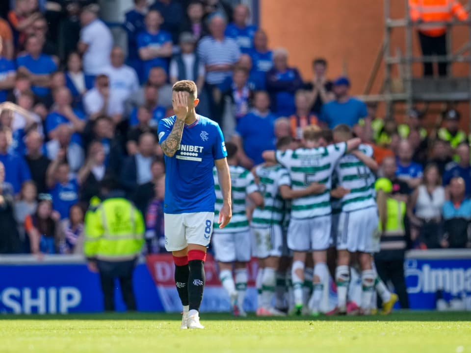 Celtic-Spieler feiern im Hintergrund einen Treffer, im Vordergrund ein Rangers-Spieler.