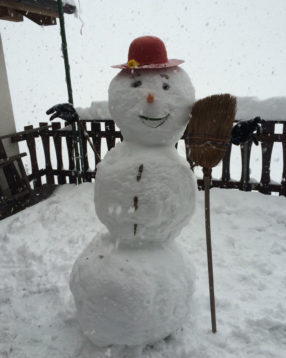 Ein mannsgrosser Schneemann mit einem Besen und einem roten Hut. Der Hut steht ihm gut.