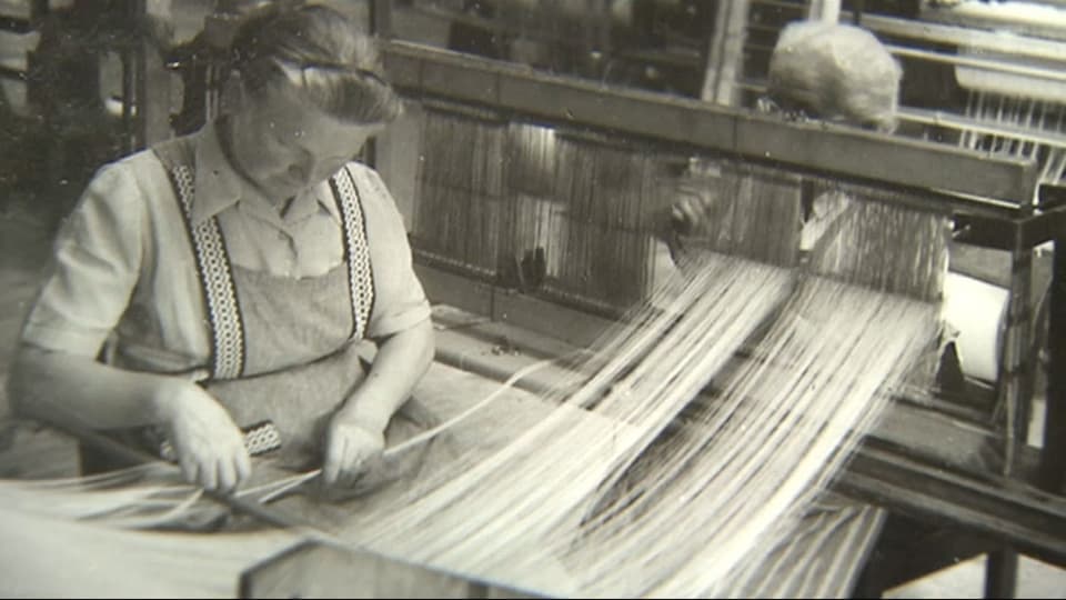 Schwarzweissbild einer Arbeiterin an einer Textilverarbeitungsmaschine.