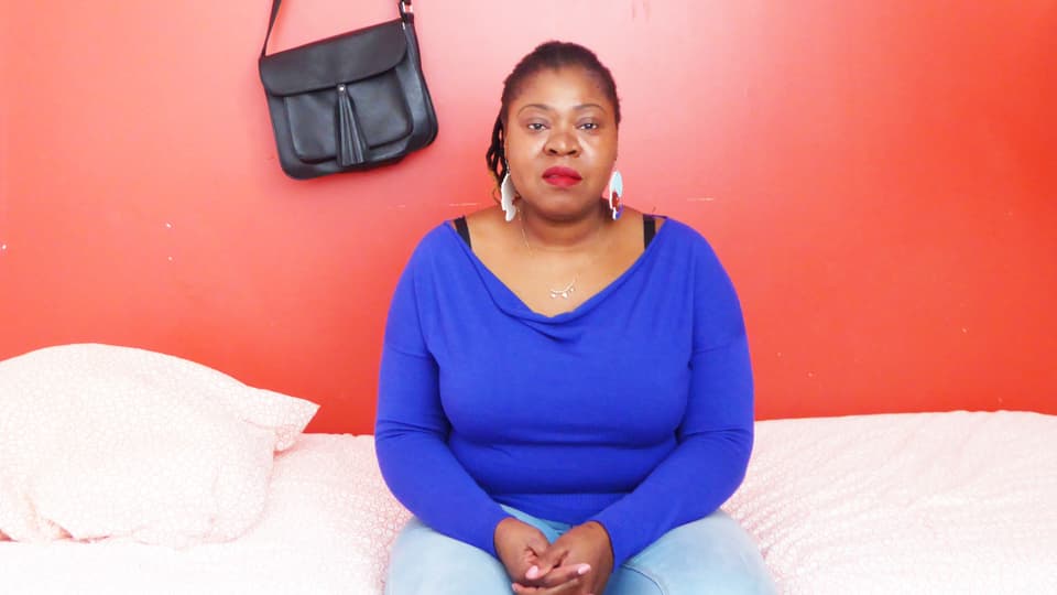 Thelma Chikwanha sitzt auf einem Bett.