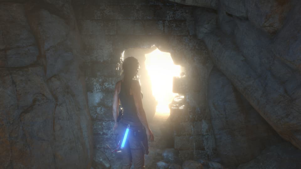 Lara Croft steht im Dunkeln vor eine Öffnung, durch die Licht scheint.