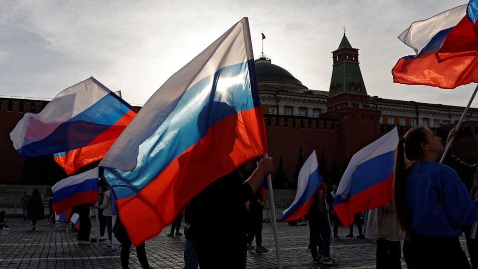 Menschen halten russsiche Flaggen in die Höhe, auf dem roten Platz in Moskau.