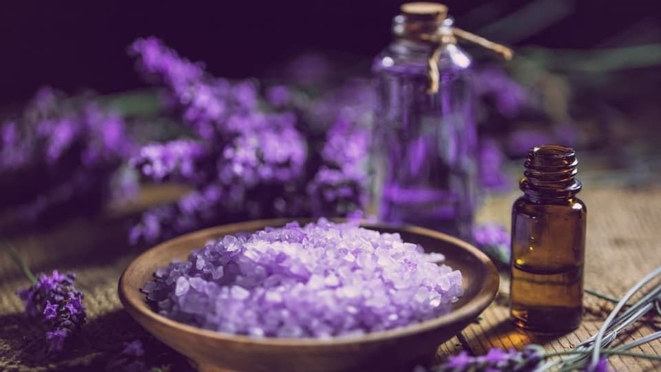 Lavendelblüten und violettes Salz neben einer Aromaflasche.
