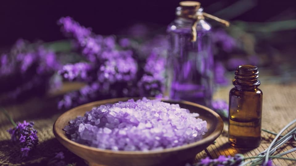 Mit Lavdendel und Co. in den Tiefschlaf? Lavendelblüten und violettes Salz neben einer Aromaflasche.
