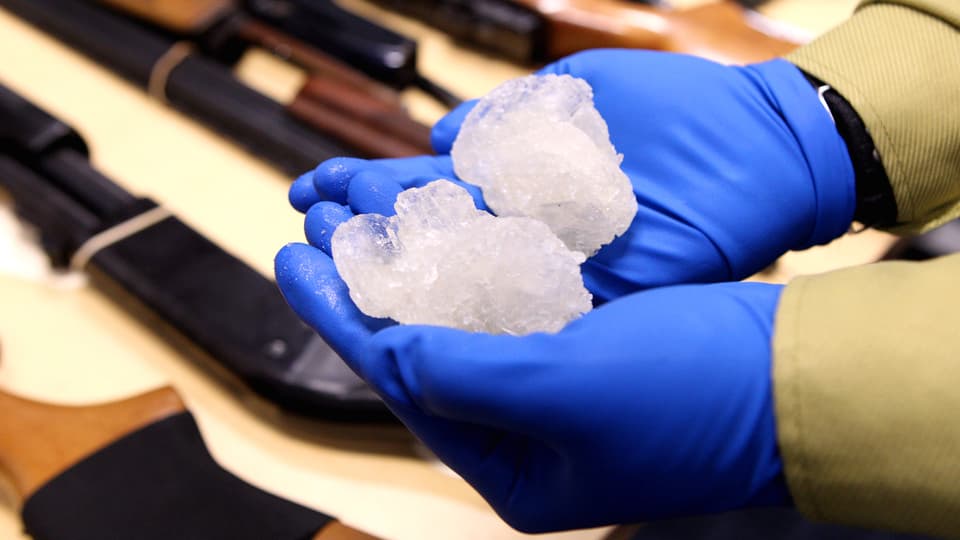 Zwei Hände in Handschuhen halten zwei Golfball-grosse, rosafarbene Meth-Kristalle.