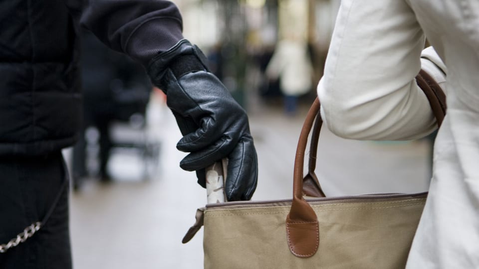 Hand mit Handschuh greift in eine Damenhandtasche.