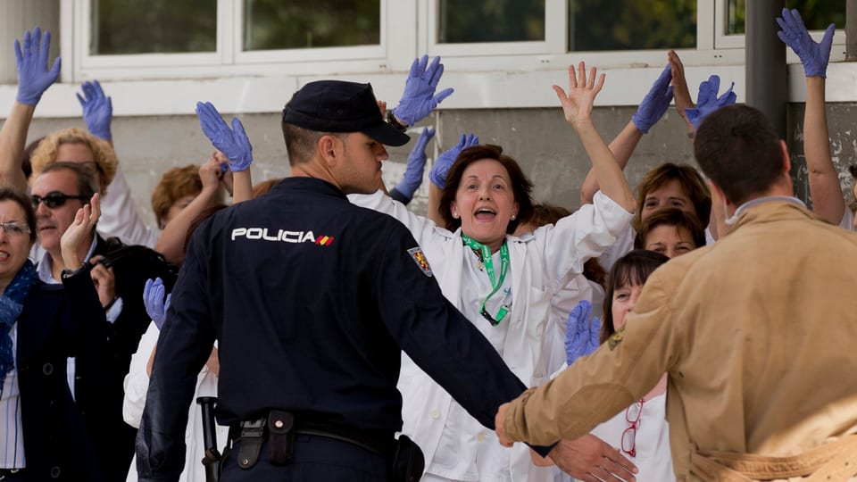 Spitalangestellte rufen und halten die Hände in die Hühe, davor bilden Polizisten eine Sperre.
