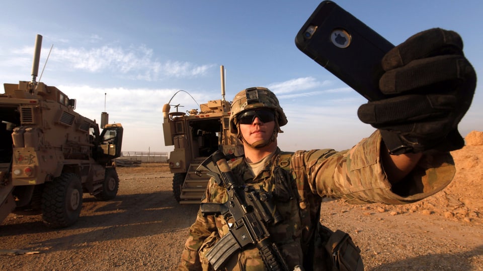Soldat macht ein Selfie, im Hintergrund zwei gepanzerte Fahrzeuge.