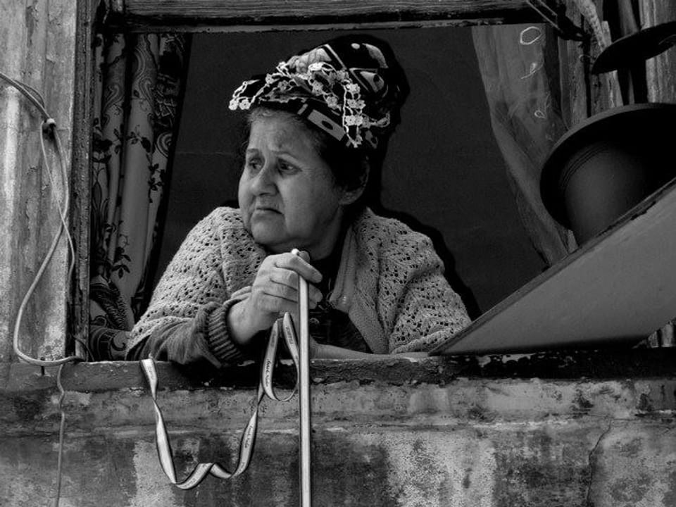 Eine ältere Frau schaut vom Balkon.
