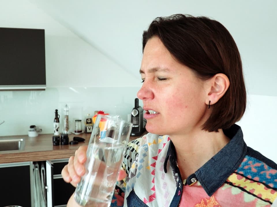 Frau hält ein Wasserglas in der Hand und rümpft die Nase